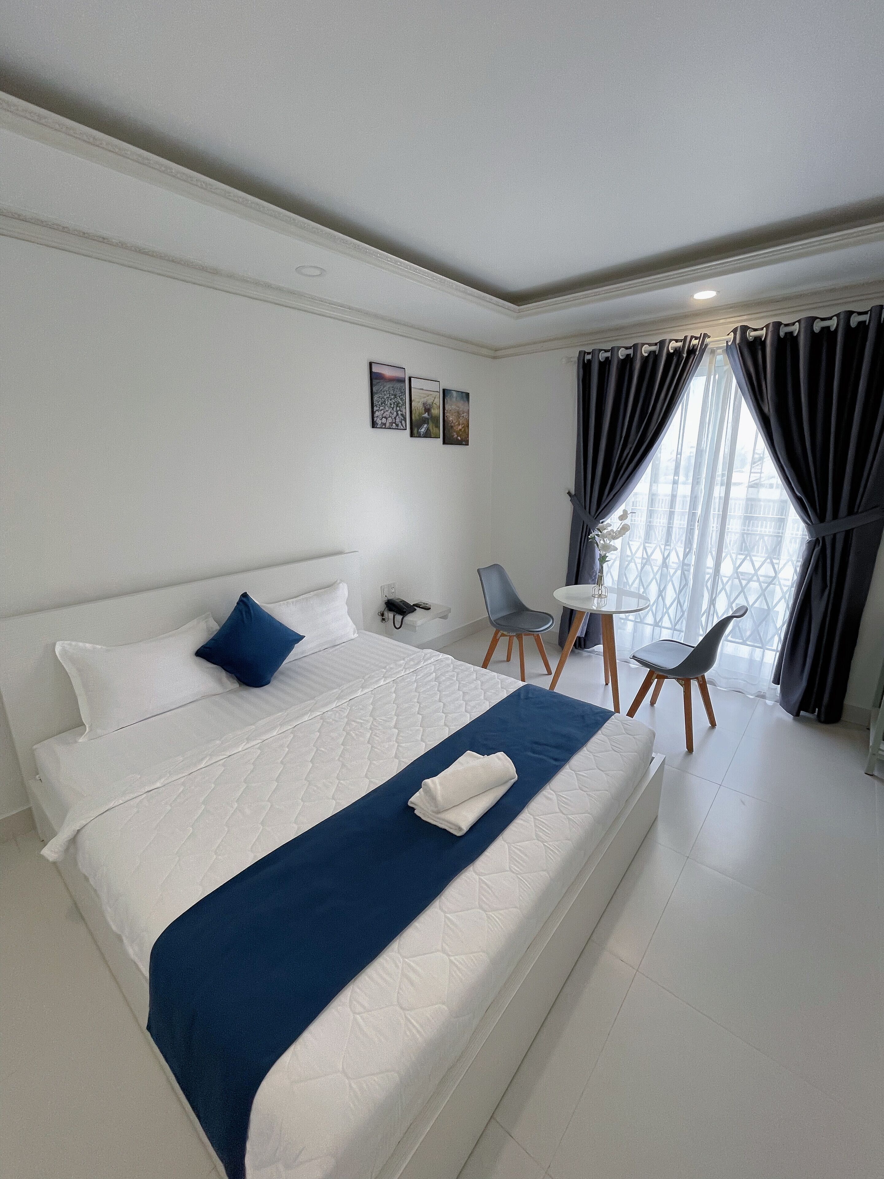 A hotel room with a large bed, a small desk, two chairs, and a window with curtains.
