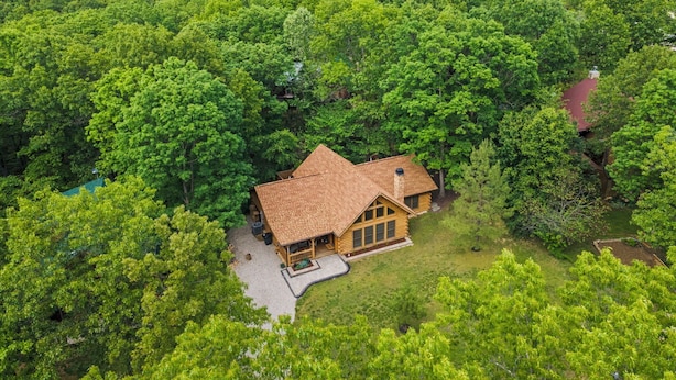 Eine Blockhütte, umgeben von dichtem Wald, mit gepflegtem Rasen und einer sauberen Auffahrt.
