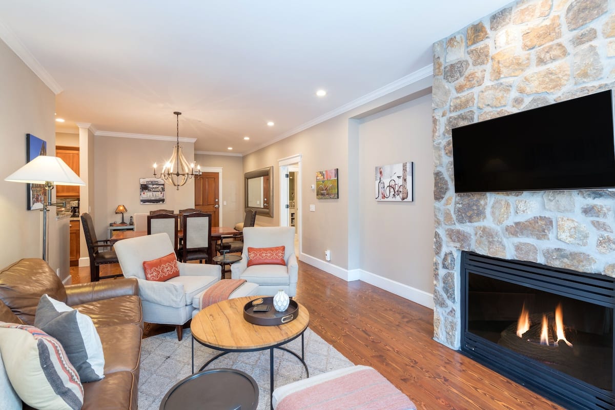 A living room with a stone fireplace, leather sofa, and a dining area in the background.