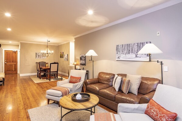 A living room with a brown leather sofa, a grey armchair, a wooden coffee table, and a dining area with a wooden table and chairs. - Alpine Lodging Telluride Ski Resort (Telluride)