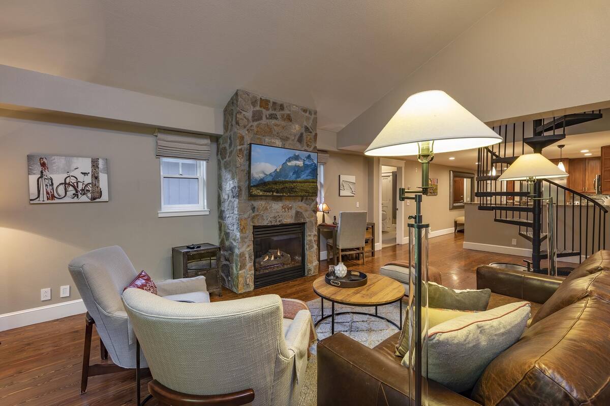 A living room with a stone fireplace, a sofa, a coffee table, and a staircase in the background.