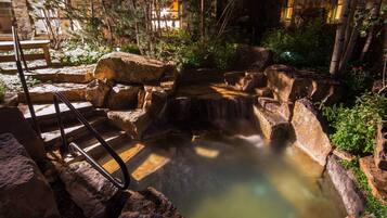 A stone water feature with a small waterfall, surrounded by rocks and greenery.