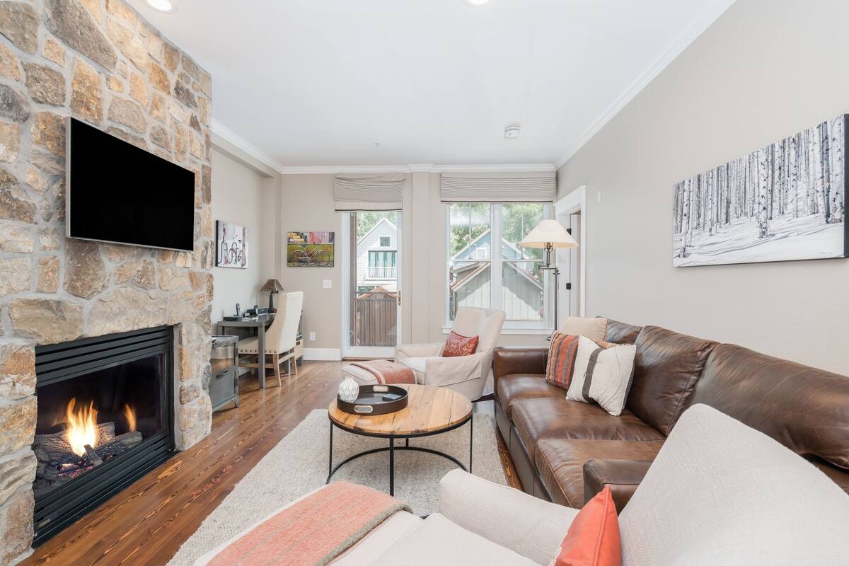 A living room with a stone fireplace, leather sofa, and a flat-screen TV mounted on the wall.