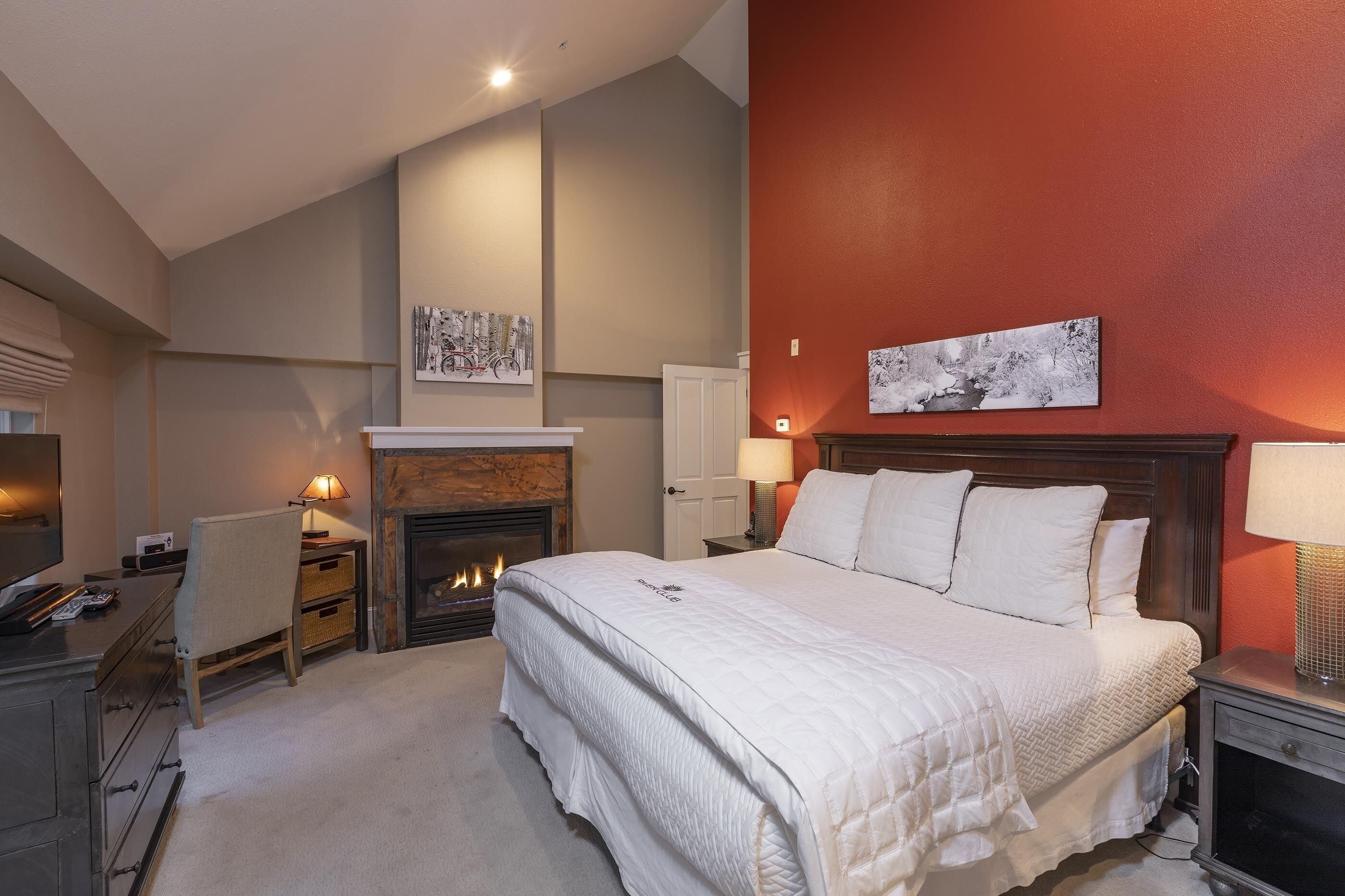 Een slaapkamer met een groot bed, een open haard, een bureau met stoel, en kunstwerken aan de wanden.