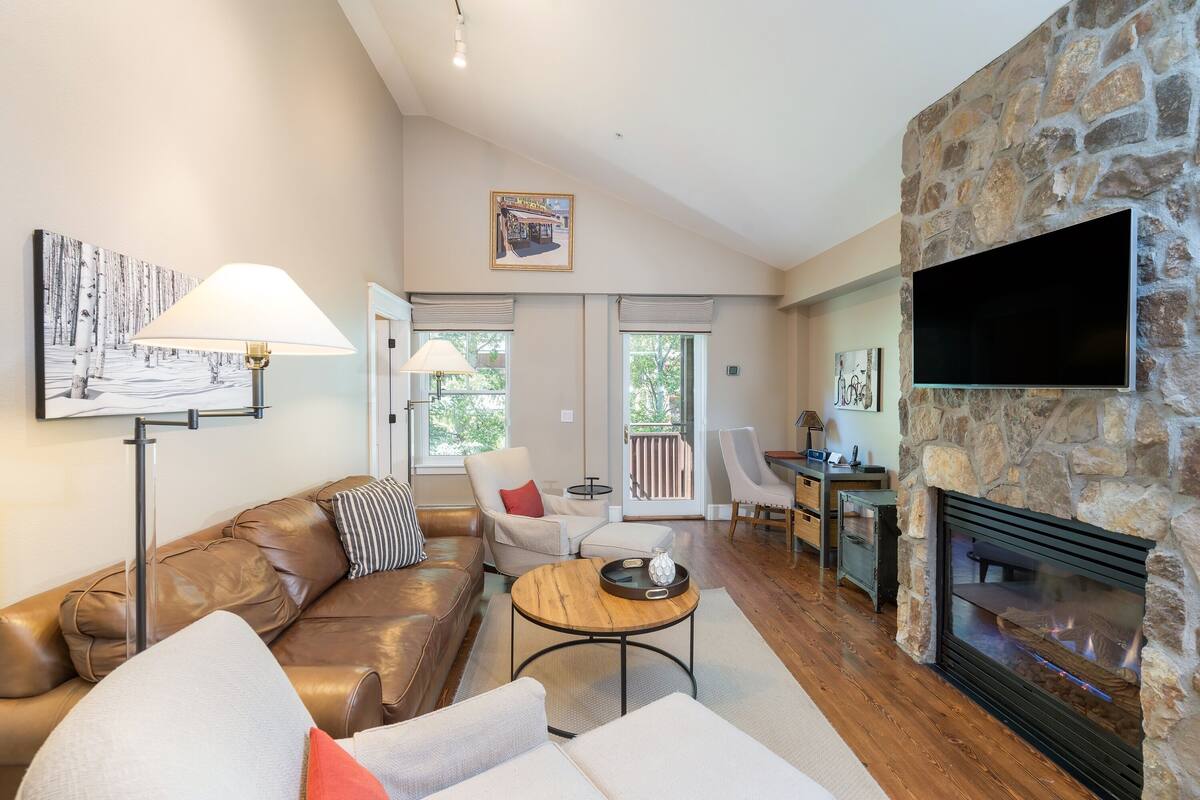 A spacious living room with a stone fireplace, leather sofas, and a flat-screen TV mounted on the wall.