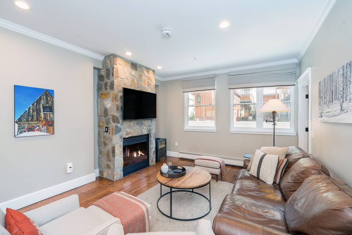 A living room with a stone fireplace, leather sofa, and a flat-screen TV mounted on the wall.