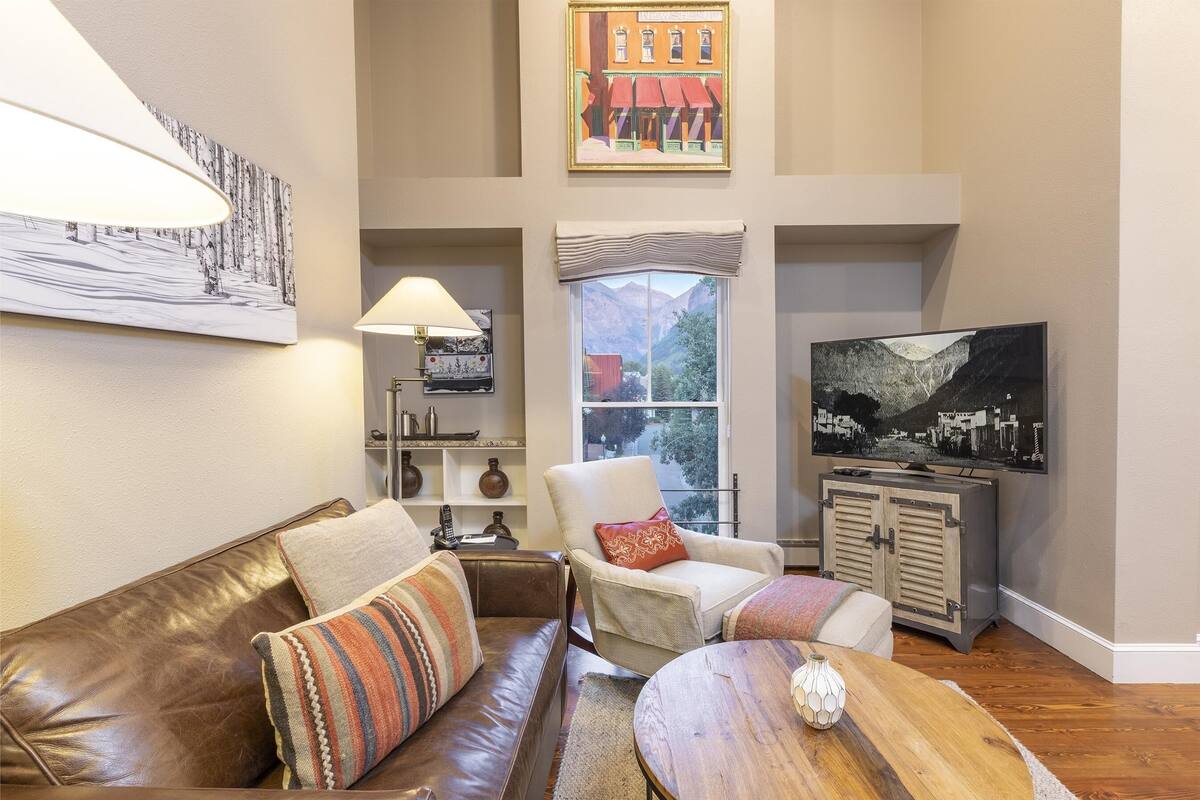 A living room with a brown leather couch, a white armchair, a wooden coffee table, a lamp, and a television.
