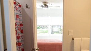A hallway leading to a bedroom with a bed, a ceiling fan, and a view of the outdoors.