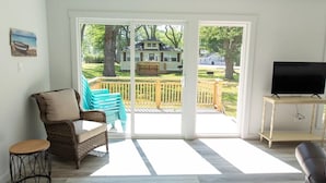 A living room with a wicker chair, a small round table, a television on a stand, and a sliding glass door leading to an outdoor deck.