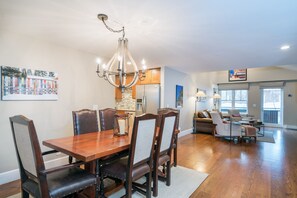 A spacious dining area with a wooden table and chairs, a chandelier, and a kitchen in the background.