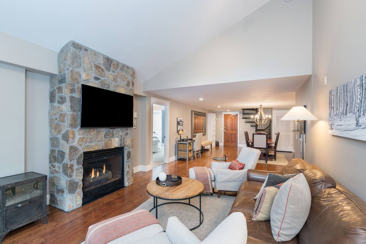 A modern living room with a stone fireplace, leather sofa, and a flat-screen TV mounted on the wall.