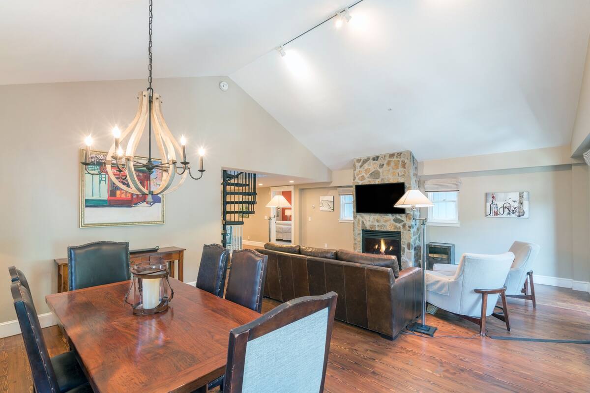 A dining area with a wooden table and chairs, a chandelier, and a stone fireplace.