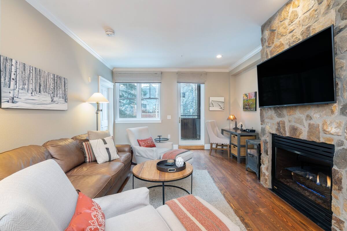 A living room with a stone fireplace, a sofa, a coffee table, and a television mounted on the wall.