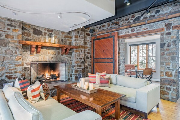 A cozy living room with a stone wall, fireplace, white sofa, and wooden coffee table. - Alpine Lodging Telluride Ski Resort - Vacation Rentals (Telluride)