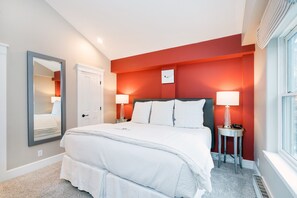 A bedroom with a bed, two bedside tables with lamps, a mirror, and a window.