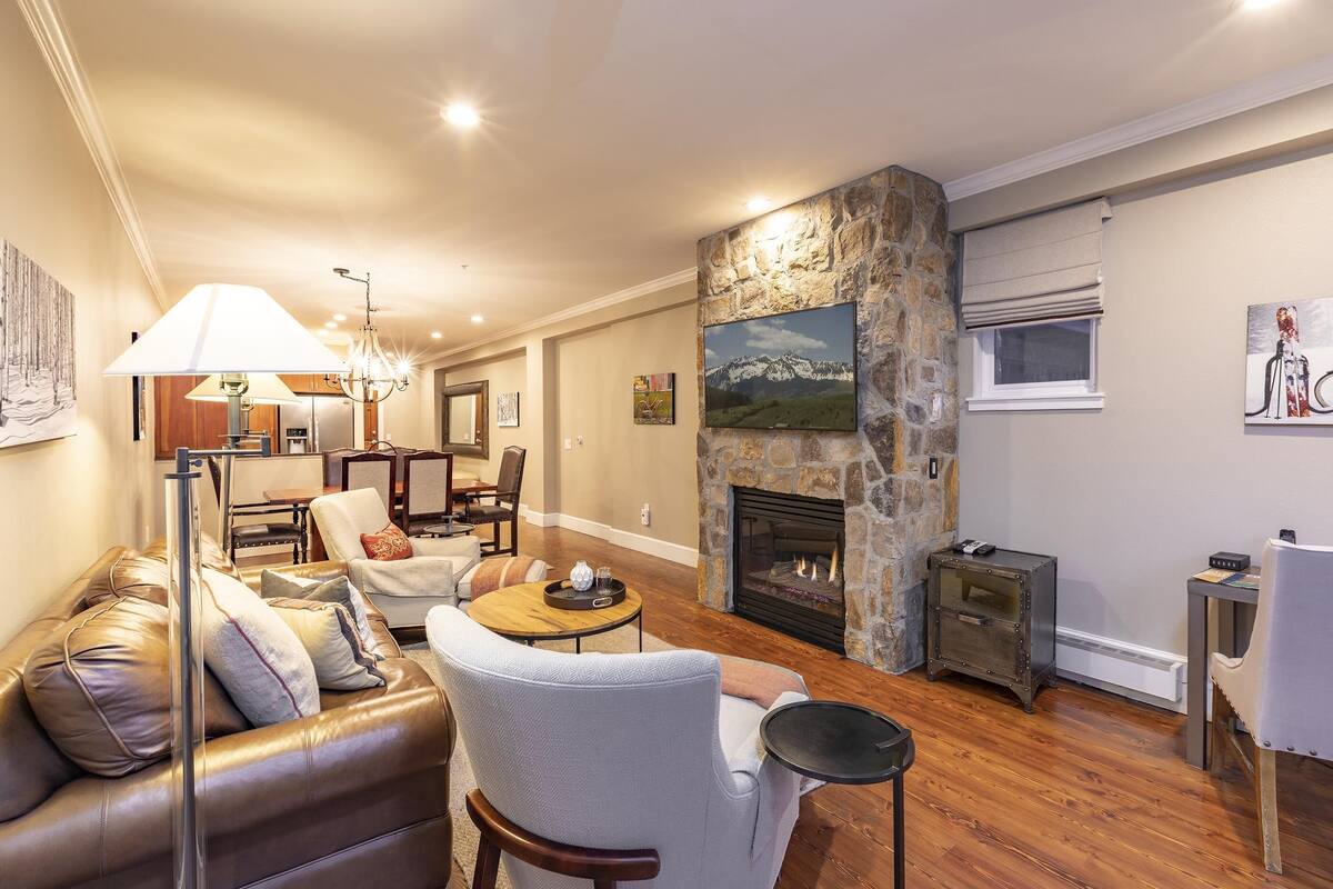 A cozy living room with a stone fireplace, leather sofa, and a dining area with a chandelier.