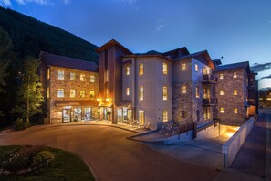 A multi-story hotel with a stone facade, multiple balconies, and a well-lit entrance area.
