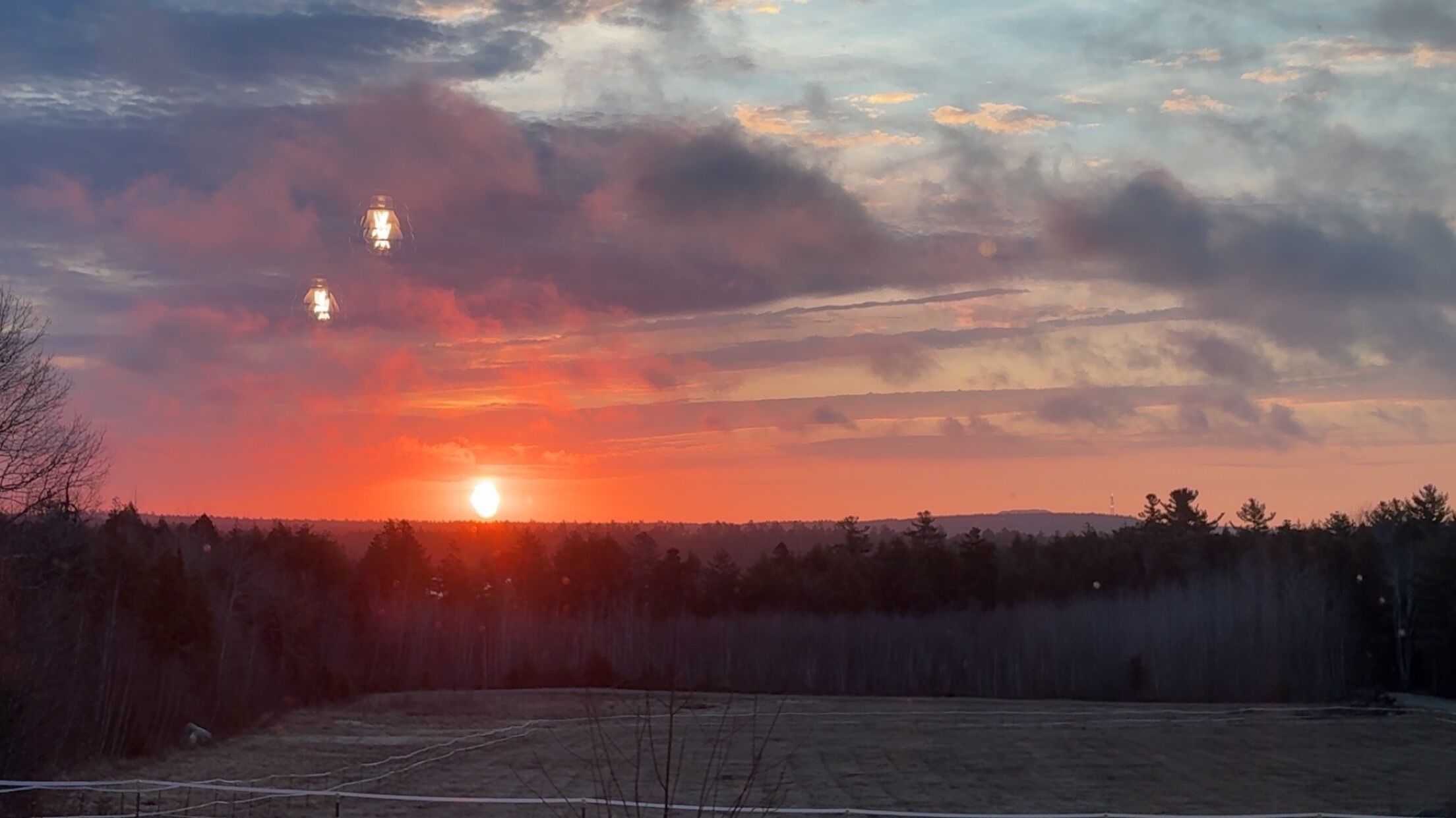 A sunset over a forested area with a clear sky and distant buildings.