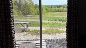 A room with a large sliding glass door leading to an outdoor area with a picnic table and a view of a green landscape. - Connect with nature - Tranquil Downeast Escape, Near Acadia & Sunrise Trail (Eastbrook)