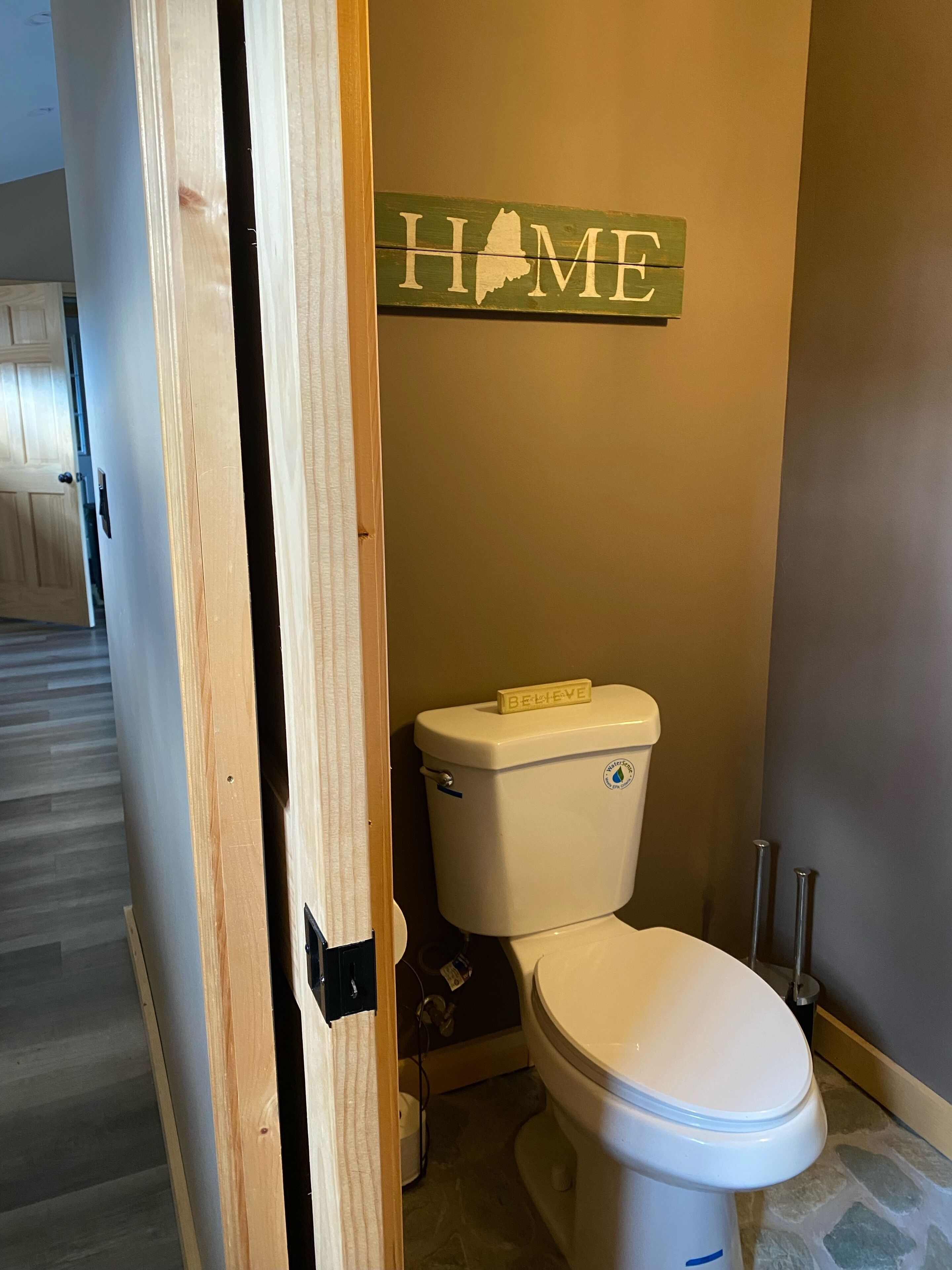 Un baño con un inodoro, un letrero de madera que dice "HOME" y un marco de puerta de madera.