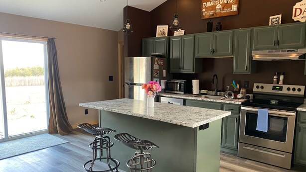 A modern kitchen with green cabinets, a large island with bar stools, a microwave, oven, and a sink. - Connect with nature - Tranquil Downeast Escape, Near Acadia & Sunrise Trail (Eastbrook)