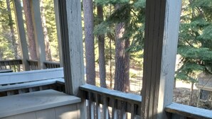 A covered outdoor seating area with a table and chairs, a lantern, and a view of trees and rocks. - Modern Contemporary Condo-Tahoe Lodge Atmosphere in Incline Village, NV. (Incline Village)