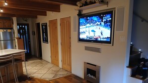 A modern kitchen with a built-in refrigerator, a dining area with a bar stool, and a TV mounted on the wall displaying a sports game. - Modern Contemporary Condo-Tahoe Lodge Atmosphere in Incline Village, NV. (Incline Village)