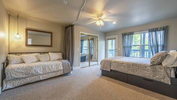 A bedroom with two beds, a ceiling fan, a large mirror, and a view of the outside through a window.