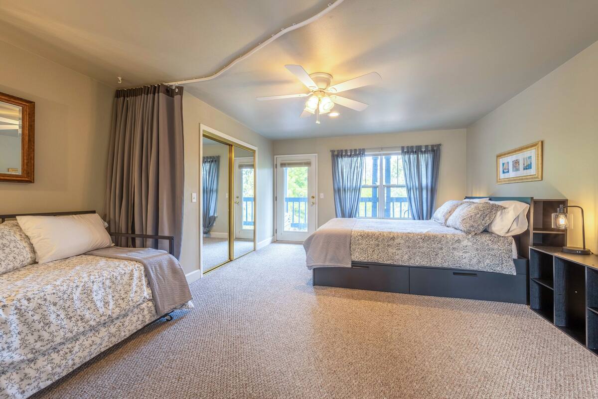 A bedroom with two beds, a ceiling fan, a nightstand, and a window with curtains.