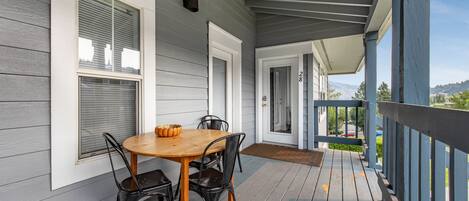 A covered porch with a wooden table and chairs, a door with a number, and a view of the outdoors.