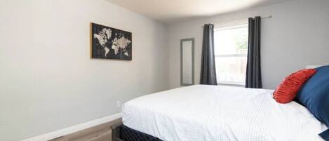 Un dormitorio con una cama, un ventilador de techo, una obra de arte con un mapa del mundo y una ventana con cortinas.