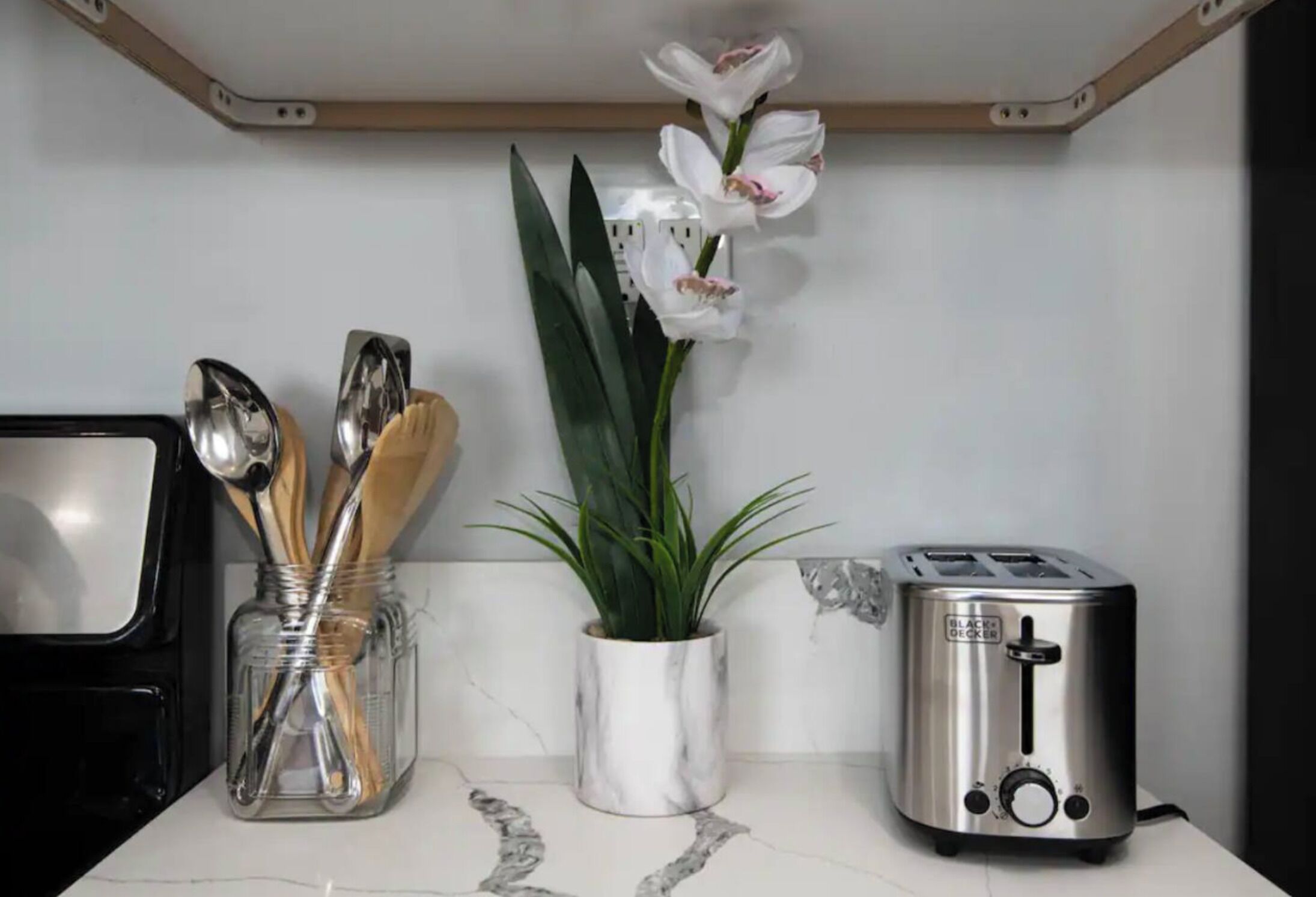 Uma bancada de cozinha com uma torradeira, uma planta em vaso de mármore e um frasco com utensílios.