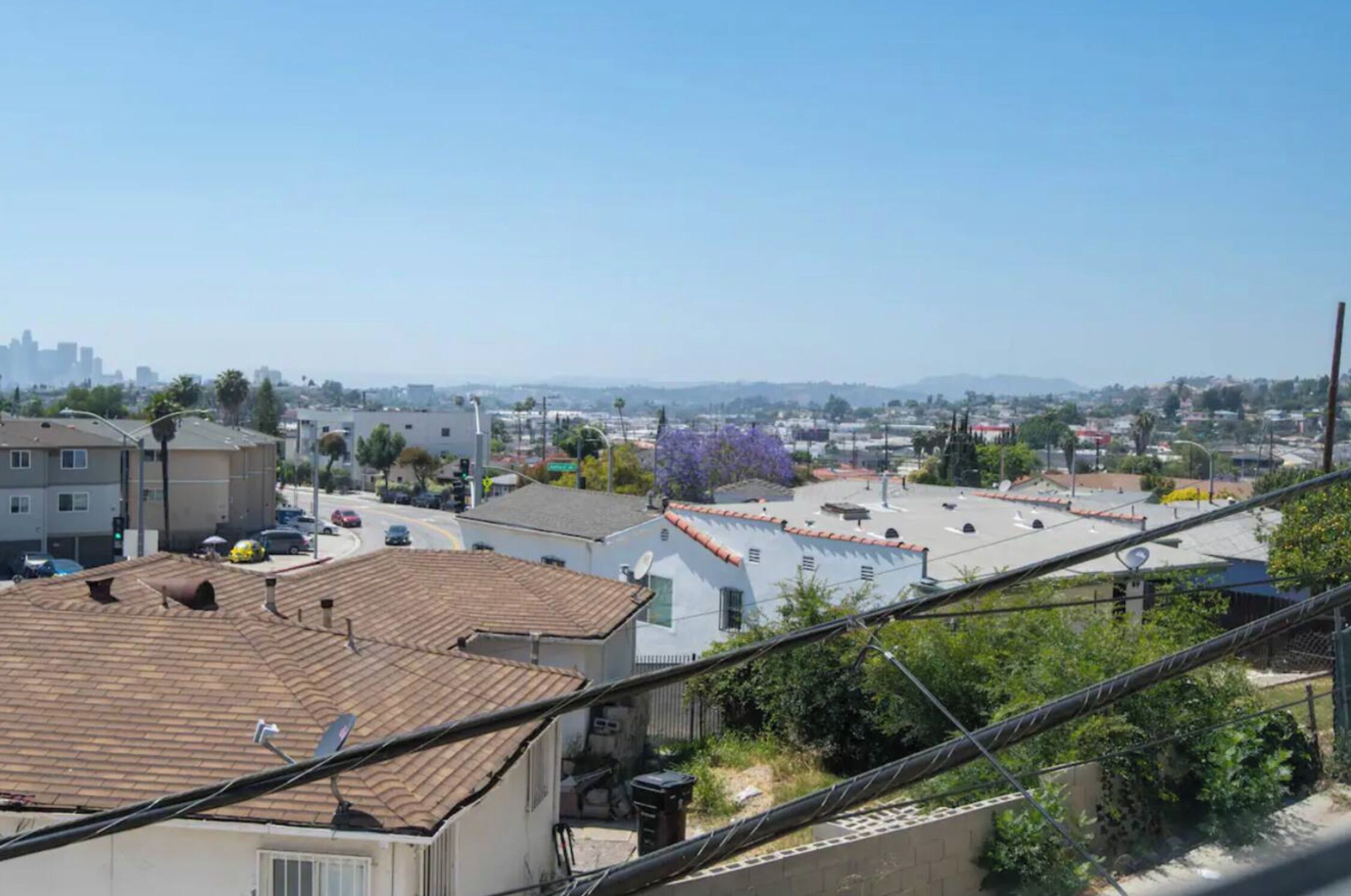 Zona residencial con vista despejada a un horizonte urbano distante, un estacionamiento y un edificio con tejado de baldosas.
