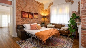 A cozy room with a brick wall, a bed, a sofa, and a large plant. - Walking distance to train stations, sporting venues and parks (Hamilton)