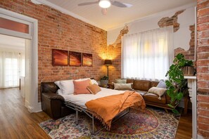 A cozy room with a brick wall, a bed, a sofa, and a large plant. - Walking distance to train stations, sporting venues and parks (Hamilton)