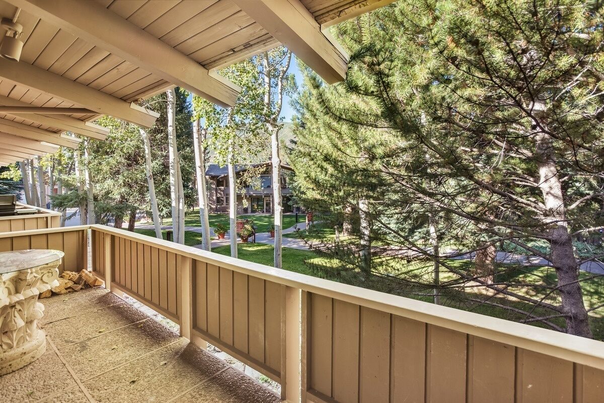 A covered balcony with a view of a well-maintained lawn and trees.