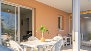Um pátio com mesa e cadeiras, um vaso de planta e uma porta de correr de vidro que dá para um ambiente interno.