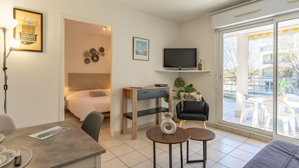 Quarto de hotel moderno com cama, escrivaninha, TV e varanda com área de estar externa.