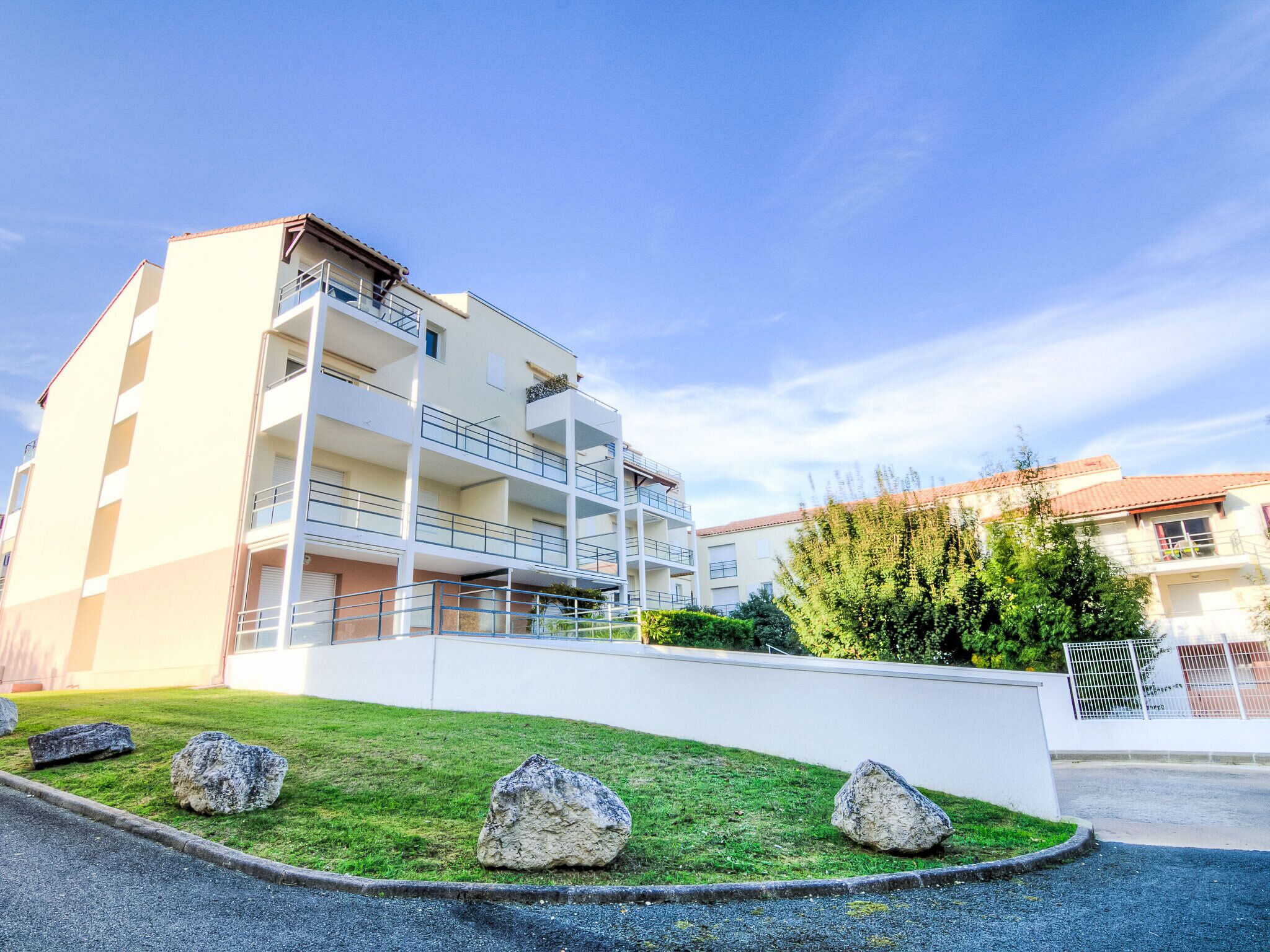 Un immeuble résidentiel à plusieurs étages, doté de balcons, d’une pelouse bien entretenue et de gros rochers au premier plan.