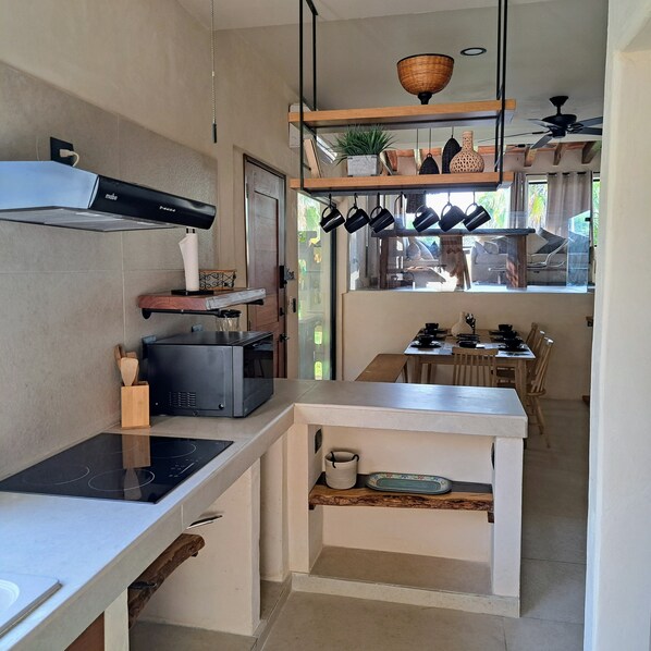 A compact kitchen with a built-in stove, a microwave, and a range hood. There is a dining area with a table and chairs, and a window providing a view of the outside.