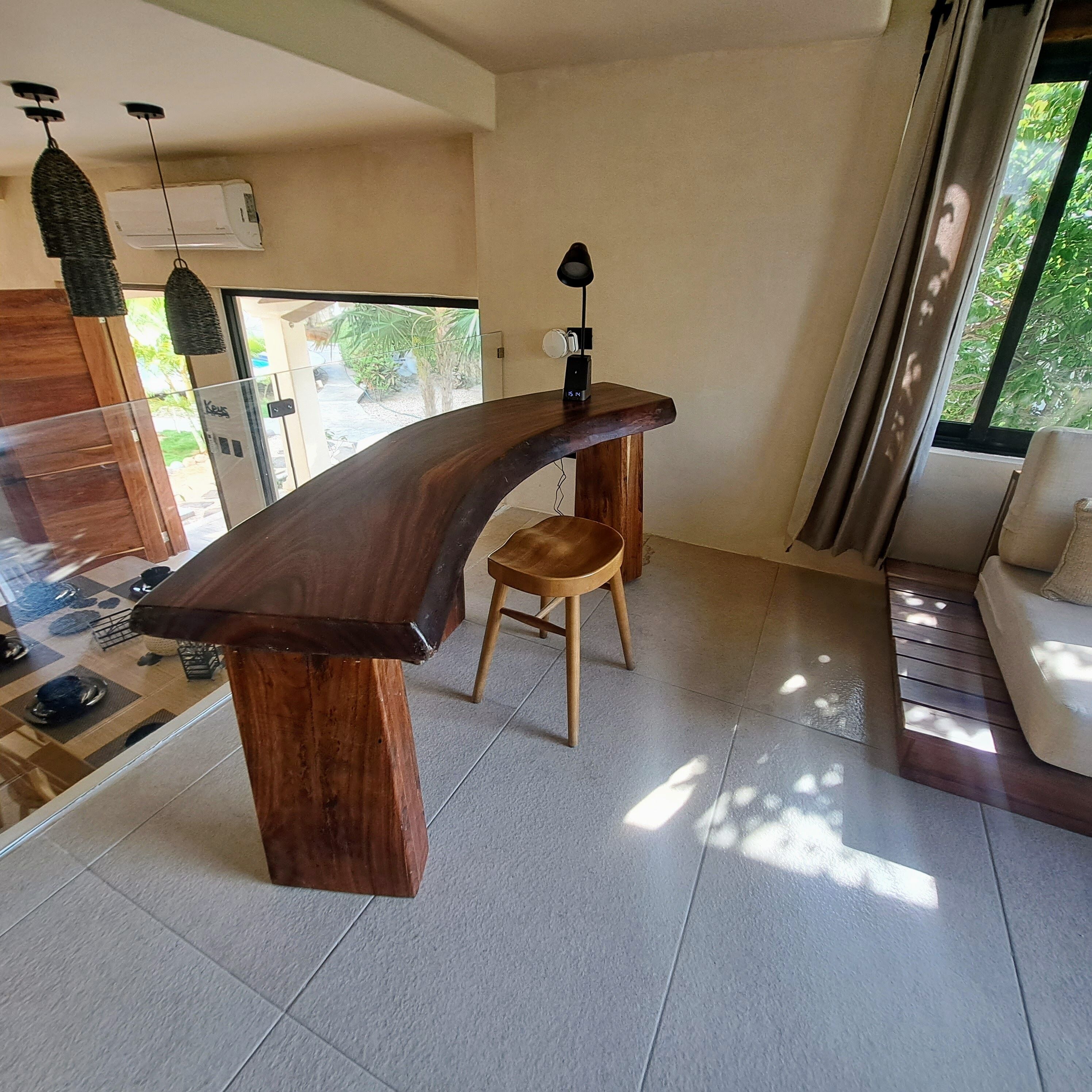 A modern kitchen with a curved wooden countertop, a wooden stool, and a pendant light.