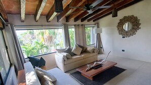 A spacious living area with a sofa, a coffee table, and a ceiling fan. There is a window with a view of greenery outside. - Cancún Energy, Tulum Spirit  Luxe & Private Stay (Cancún)