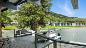 Una terrazza con posti a sedere all'aperto, vista su un lago e una collina con edifici.