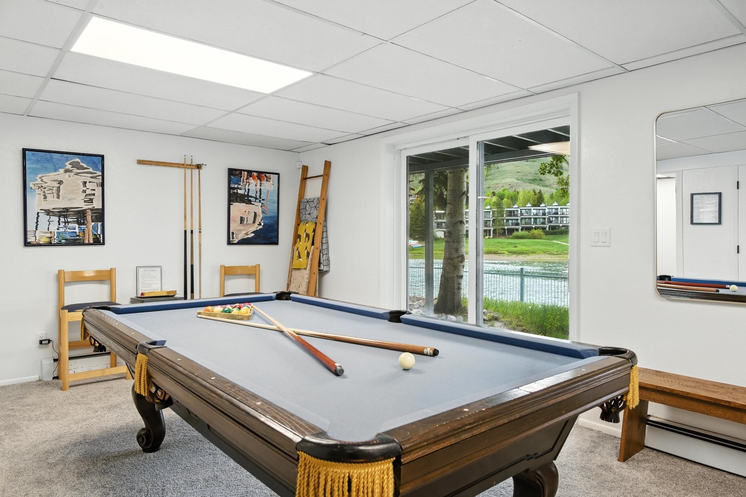 A pool table in a room with white walls, a large window, and paintings.