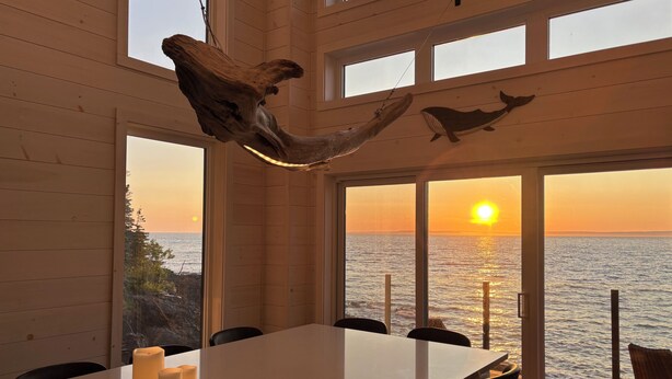 Un comedor con una mesa, sillas, velas y vistas al atardecer sobre el océano.