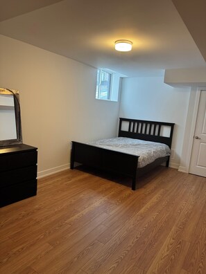 A bedroom with a bed, a dresser, a window, and a door. - Newly Built Basement Suite – Comfort & Convenience (Markham)
