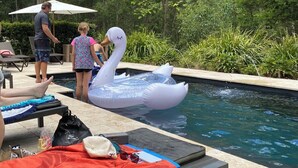 Ein Swimmingpool mit Schwimmreifen in Form von Schwänen, Liegestühlen und einer Person am Pool.
