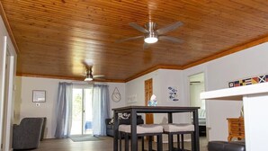 A spacious living room with a wooden ceiling, a dining table with four chairs, a sofa, and a patterned rug. - LakePointe Shores # 7 Welcoming 3-bedroom cottage in Madison on the Lake (Madison)