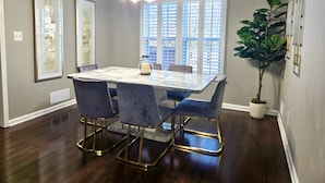 Un coin repas avec une table en marbre, des chaises en velours bleu, un lustre et une plante en pot.
