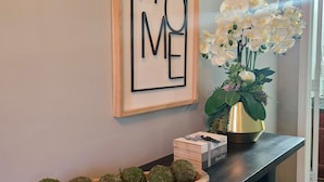 Une console en bois surmontée d’un cadre portant l’inscription « HOME », d’un vase avec des fleurs blanches et d’un plateau contenant des boules vertes.